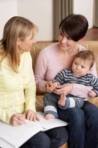 Mother With Baby Talking With Health Visitor At Home