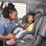 young, black mom lovingly buckling her child into a car seat.