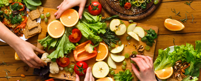 fresh vegetables and fruits cut up and laid out beautifully on a table with hands touching the oranges.
