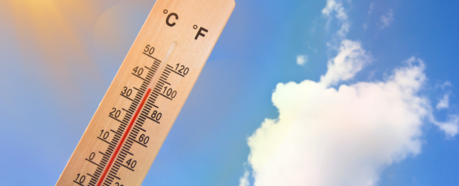 image of a thermometer being held up against a blue sky with the sun and cloud in the distance and shows the temperature is around 100 degree Farenheit