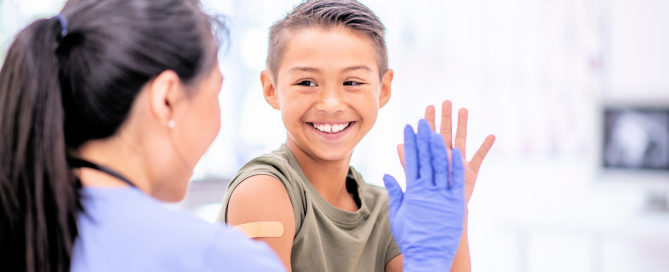 image of young boy at a doctors office and giving a high five to his provider. He is smiling big and we see the back of the provider and her hand in a medical glove.