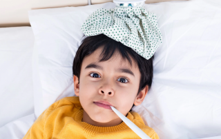 image of a young boy around 5 laying in bed with an ice pack on his head and a thermometer in his mouth to portray a sick child