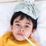 image of a young boy around 5 laying in bed with an ice pack on his head and a thermometer in his mouth to portray a sick child