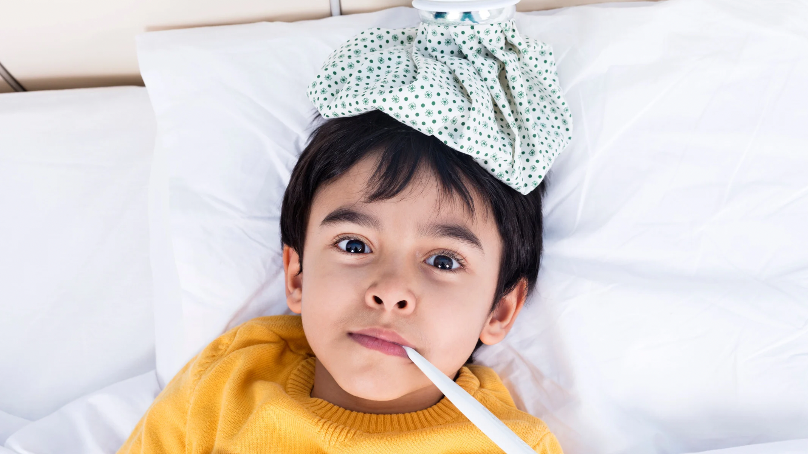image of a young boy around 5 laying in bed with an ice pack on his head and a thermometer in his mouth to portray a sick child
